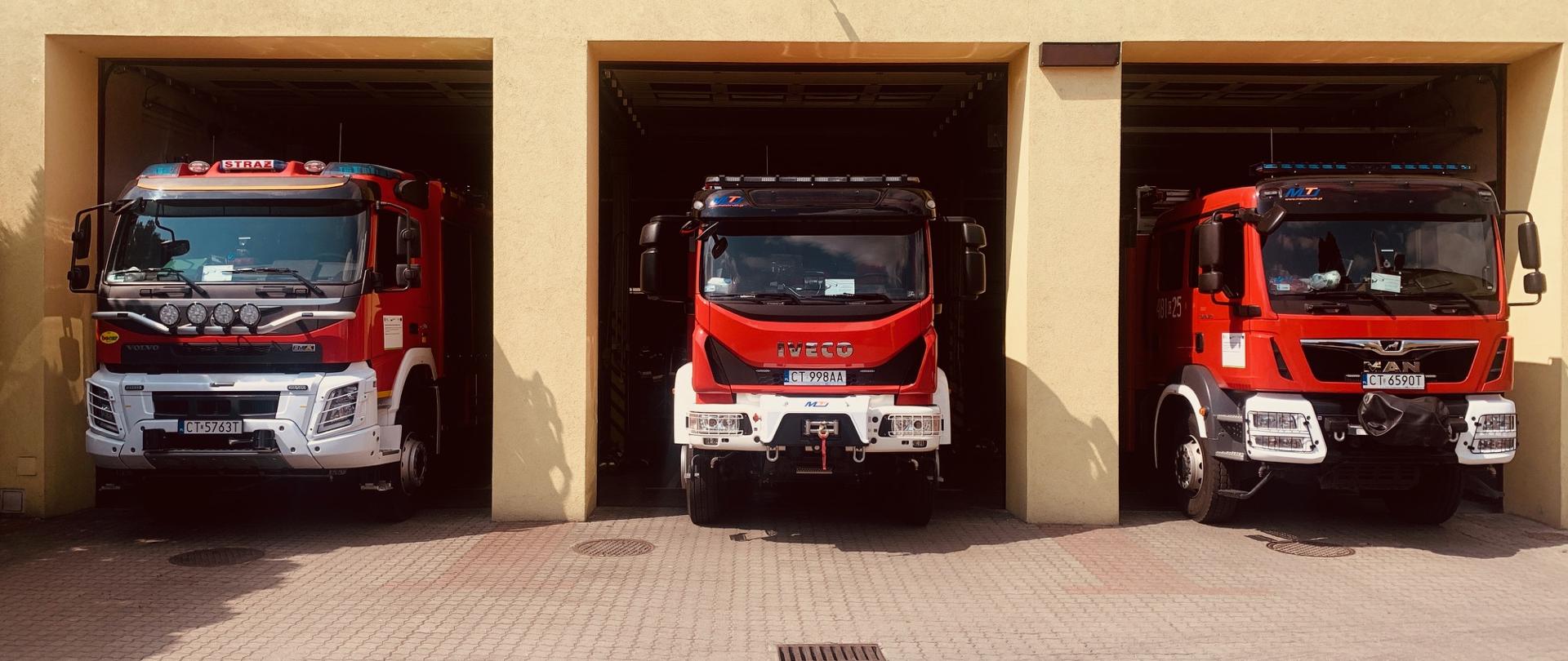 Otwarte bramy garażowe a w nich stoją 3 wozy strażackie