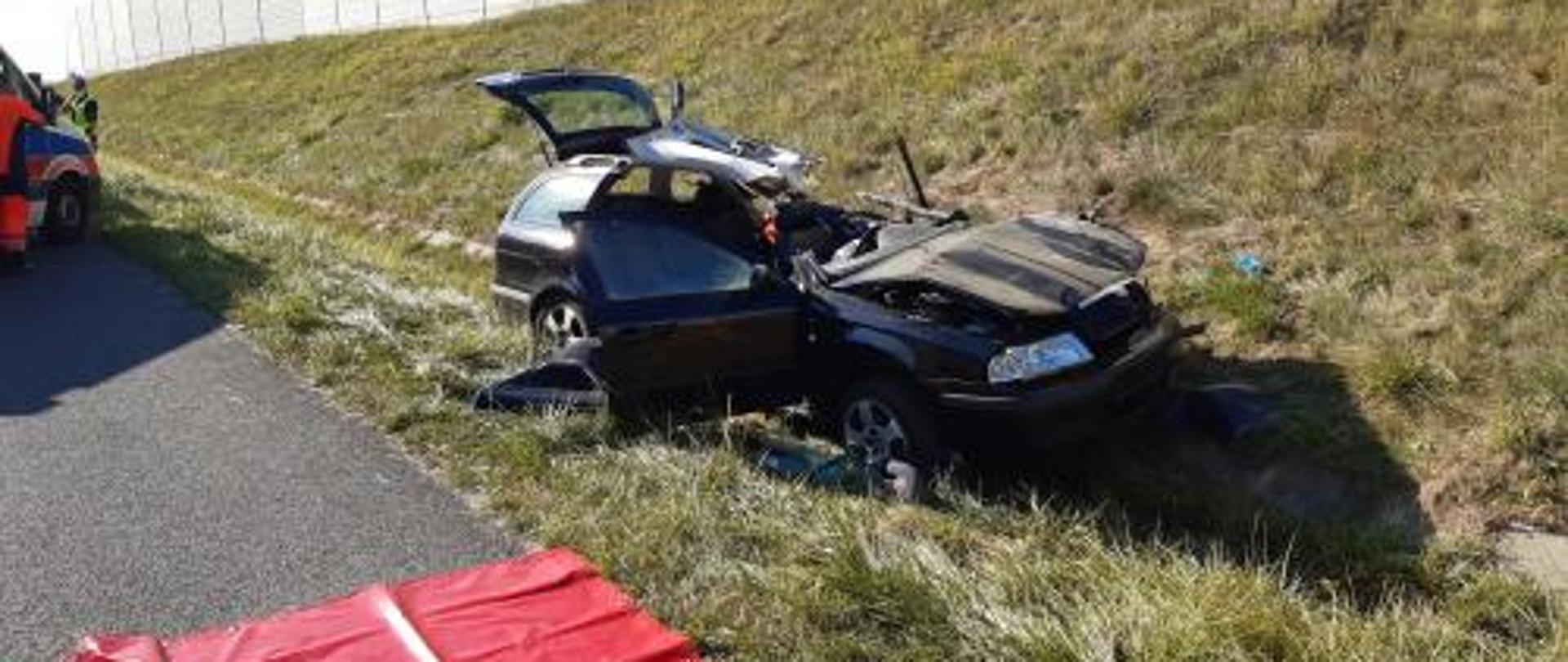 Samochód osobowy poza drogą w rowie po wypadku. Widoczne duże zniszczenia karoserii pojazdu.