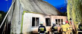 Na zdjęciu widać strażaków z wężem gaszących spalone meble wyrzucone z domu.