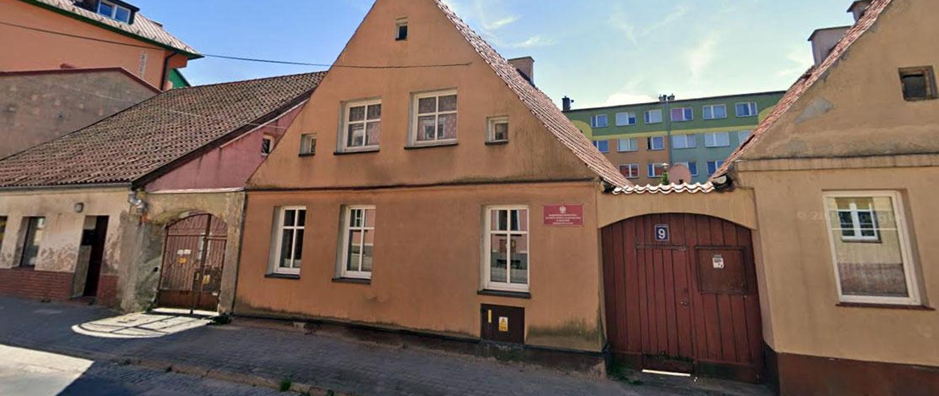 Niski dom z charakterystycznym trójkątnym dachem, usytuowany przy samej ulicy