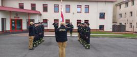 Uroczysta zmiana służby z okazji Dnia Flagi Rzeczpospolitej Polskiej. Zmiany służbowe stoją naprzeciw siebie. Na szczycie pododdziału stoi Komendant Powiatowy Państwowej Straży Pożarnej w Człuchowie st. bryg. Radosław Batruch. Poczet flagowy stoi przy maszcie, następuje uroczyste podniesienie flagi państwowej.