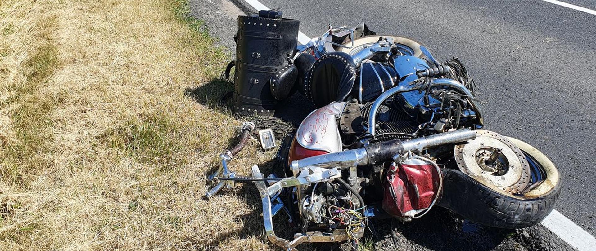 Na poboczu drogi krajowej NR 62 leży uszkodzony motocykl marki Honda, który brał udział w wypadku. za motocyklem stoi biały pojazd z niebieskimi i czerwonymi pasami widoczny napis AMBULANS, pojazd ma otworzone prawe drzwi. Po drugiej stronie drogi w przydrożnym rowie znajduje się uszkodzony samochód osobowy, który brał udział w wypadku