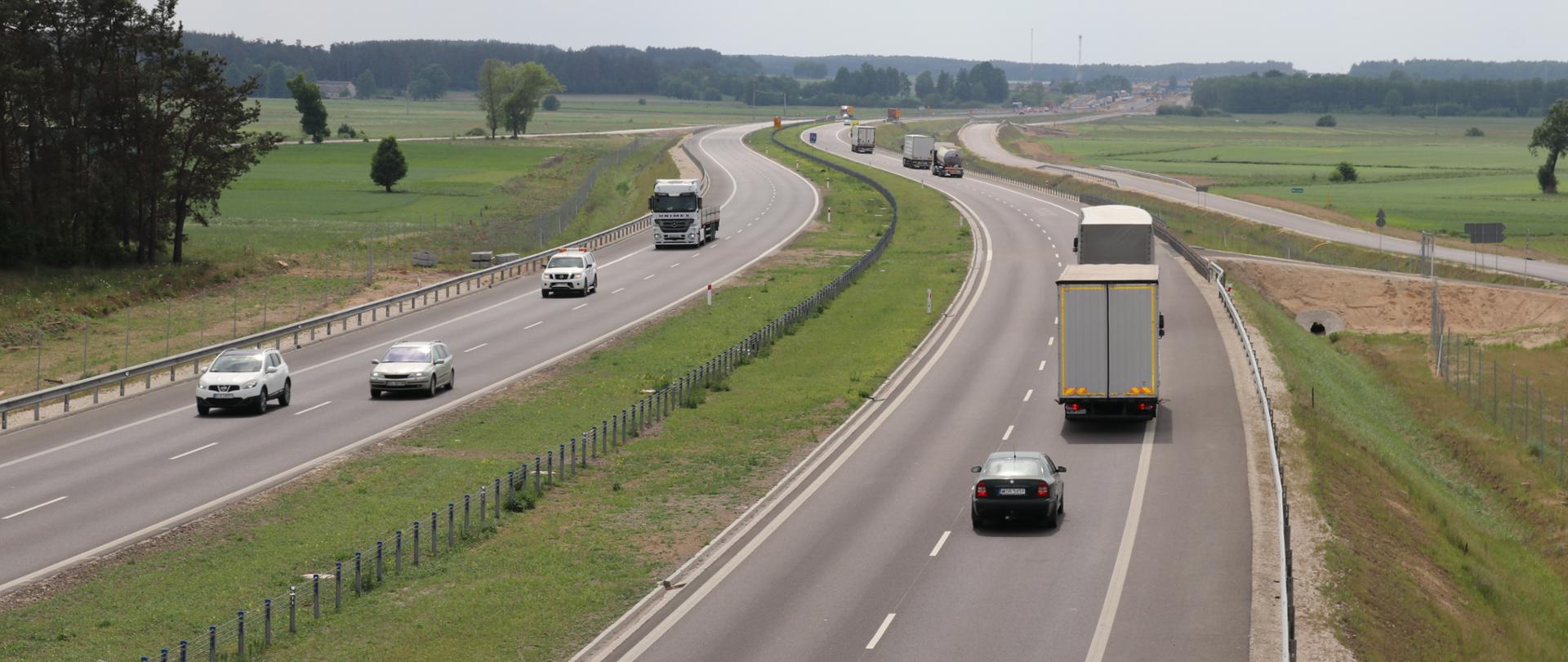 Dwujezdniowa droga ekspresowa wijąca się po horyzont, a na niej samochody jadące w przeciwnych kierunkach 