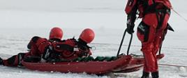 Dwóch strażaków na saniach lodowych ciągniętych przez za uchwyty sań.