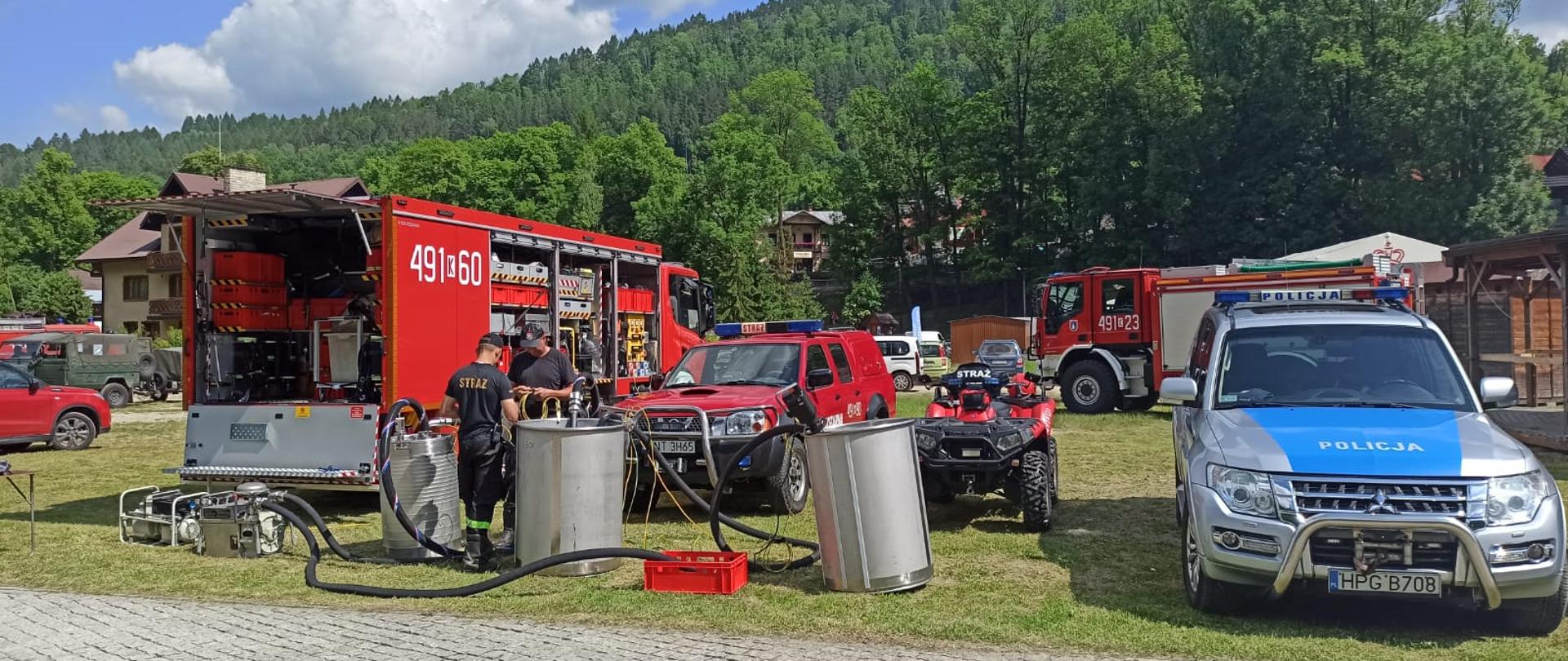 na tle zalesionych stoków dwa pojazdy samochód ratownictwa chemiczno ekologicznego i policyjny, przed samochodem rozstawione beczki do zbierania i separacji substancji chemicznych podczas działań