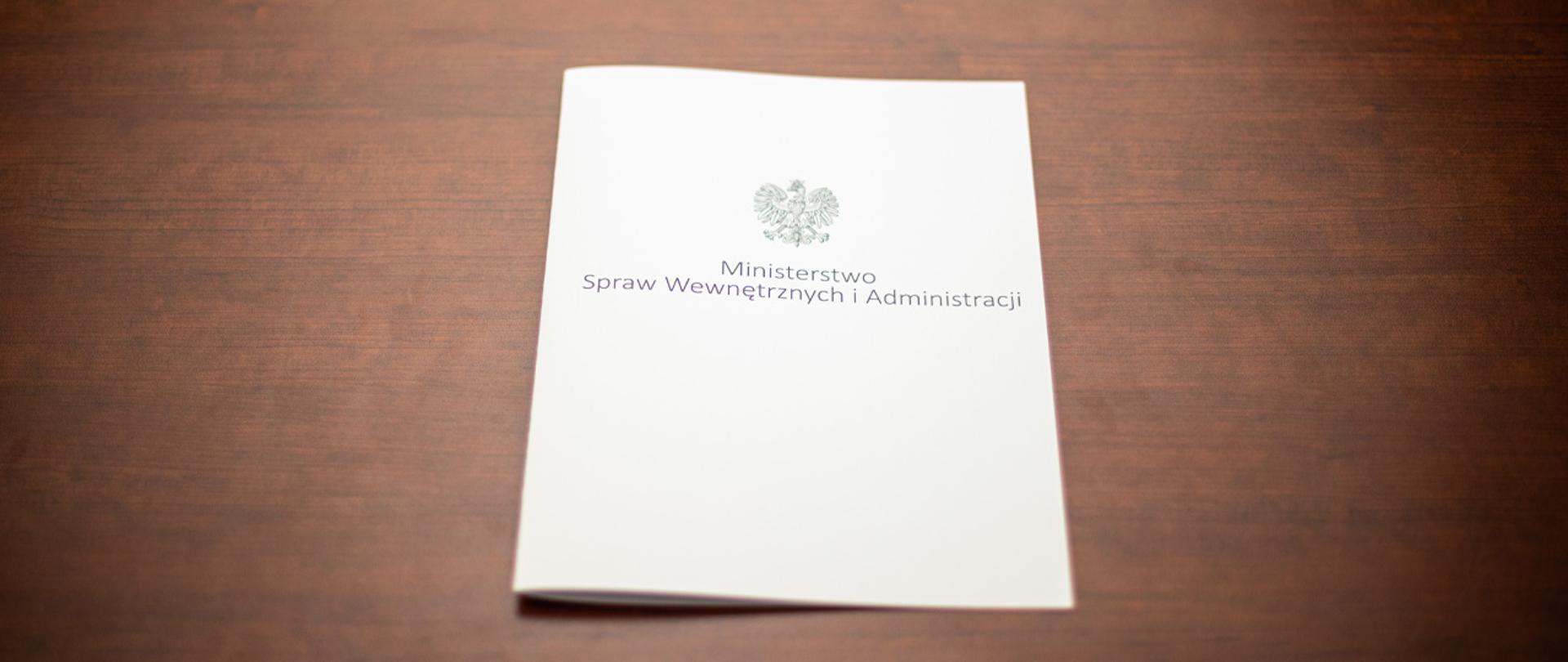 Na zdjęciu widać leżącą teczkę z napisem "Ministerstwo Spraw Wewnętrznych i Administracji" i orłem z godła narodowego.