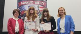 Zdjęcie przedstawia nagrodzone uczennice z dyplomami wraz z nauczycielką i organizatorką Konkursu. Uśmiechnięte osoby stoją na tle baneru z napisem „Konkurs Wiedzy 250-lecie Deklaracji Niepodległości USA (1776–2026)”, z grafiką amerykańskiej flagi i Statuy Wolności. 