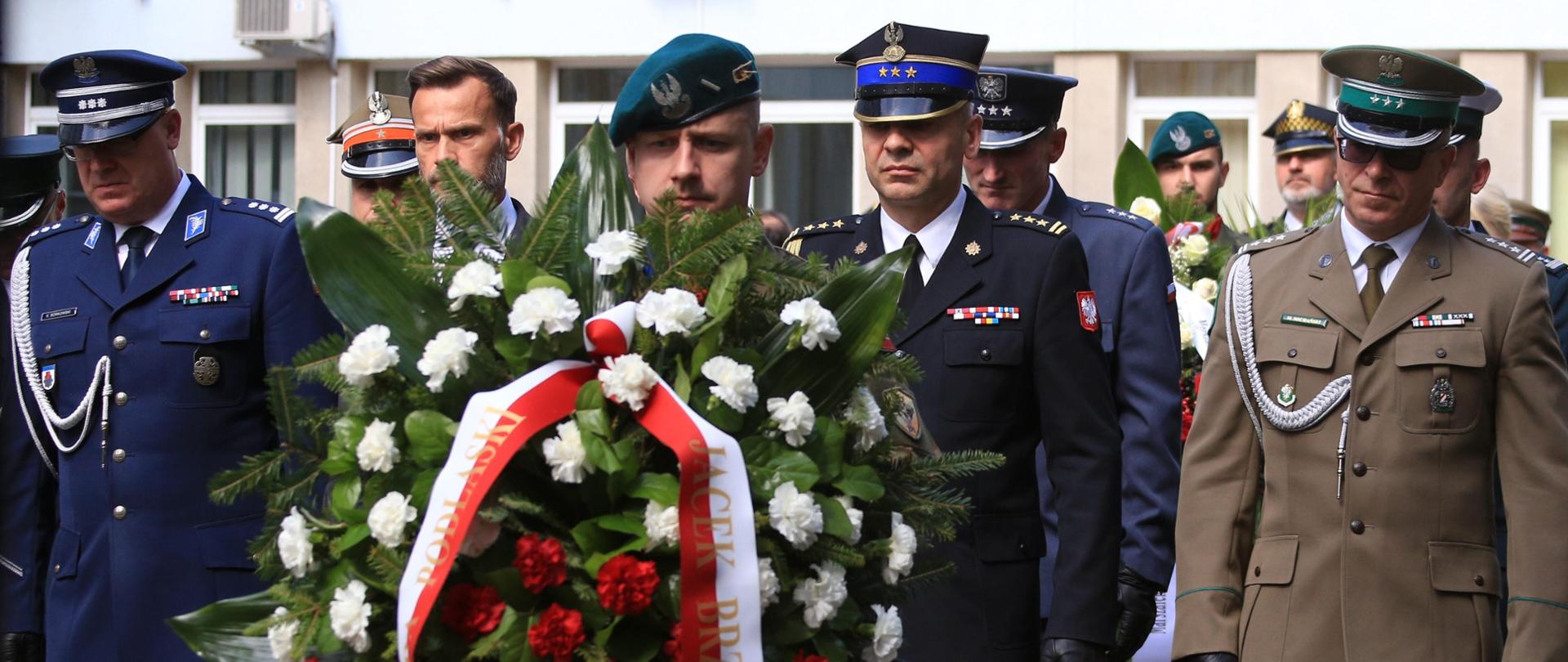 81. rocznica wybuchu Powstania w Białostockim Getcie - przedstawiciele służb w szeregu asystując Wojewodzie Podlaskiemu Podczas złożenia kwiatów pod pomnikiem. Złożenie kwiatów.