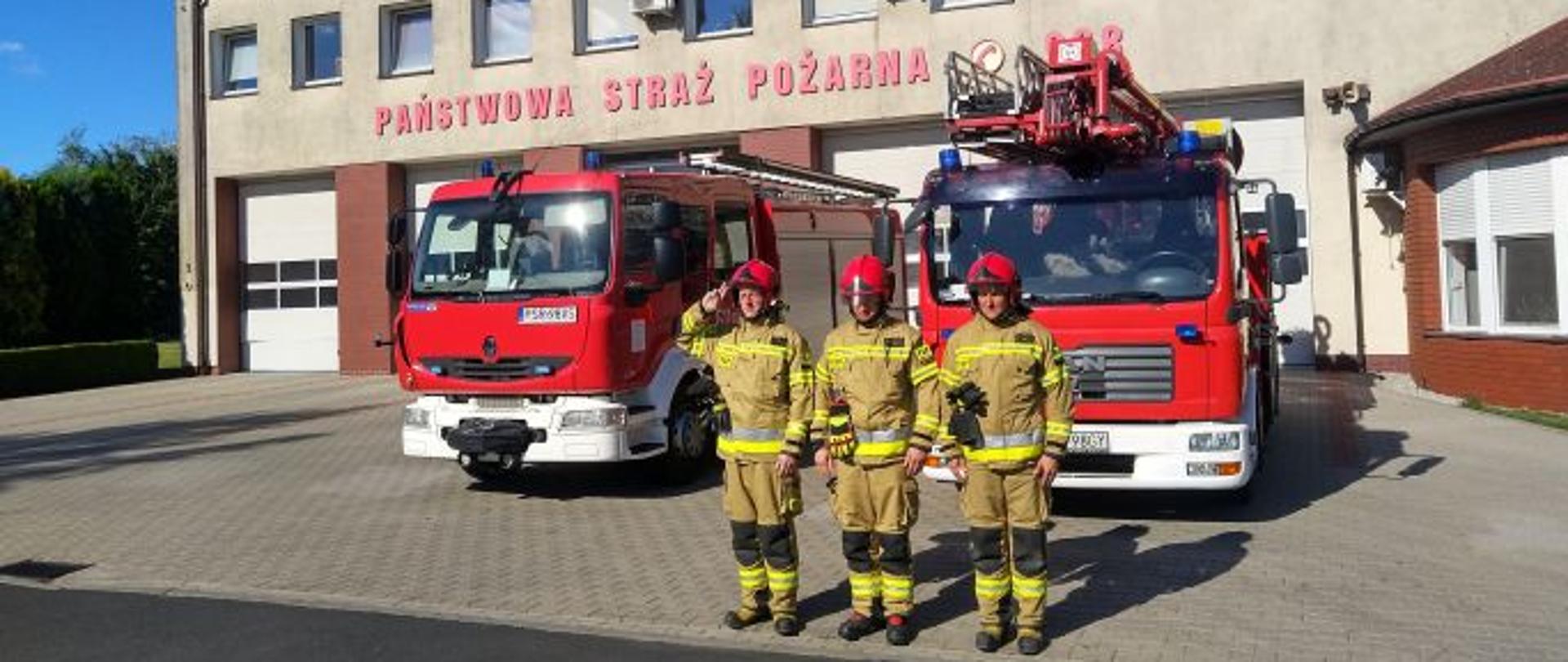 Strażacy stoją na tle samochodów gaśniczych, oddają honor z okazji 76 rocznicy wybuchu Powstania warszawskiego