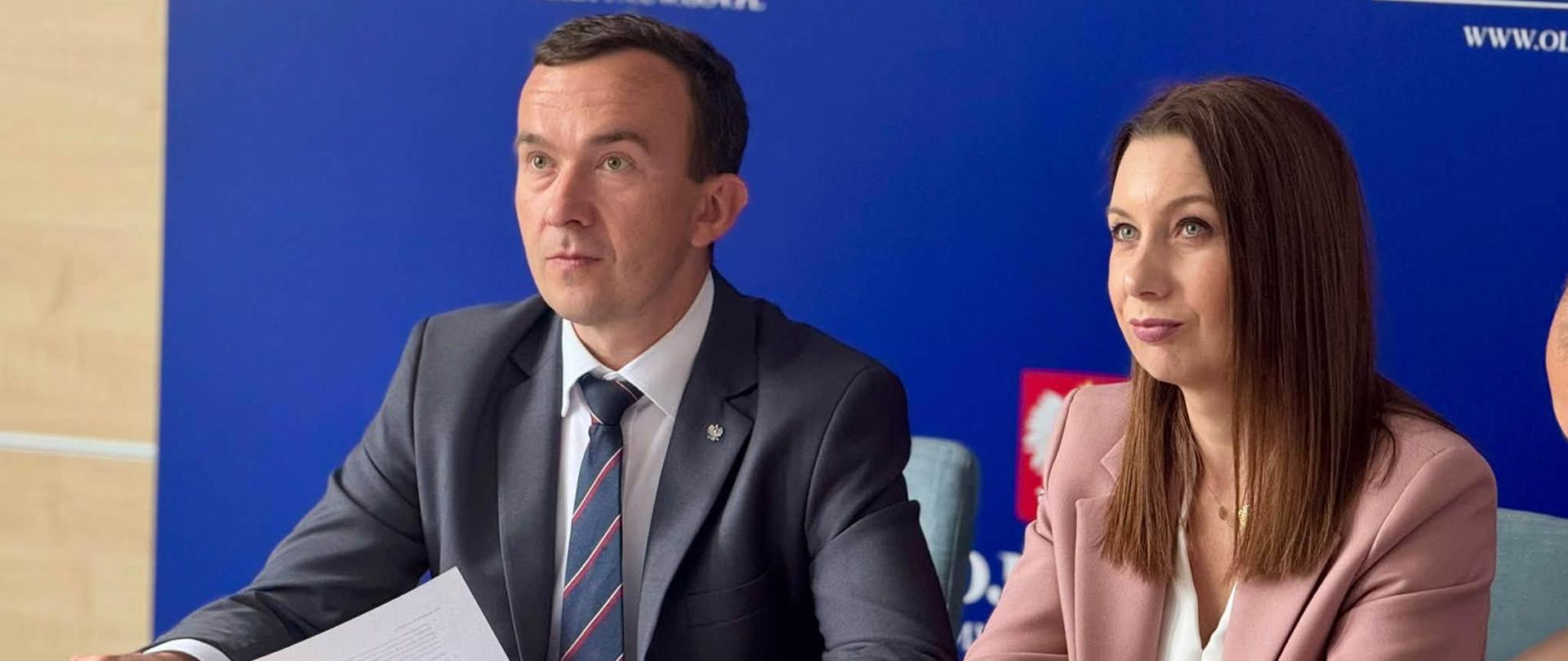 mężczyzna w garniturze, wicewojewoda, oraz kobieta w różowej marynarce, dyrektor generalny, siedzą przy stole konferencyjnym patrzą w kierunku monitorów 