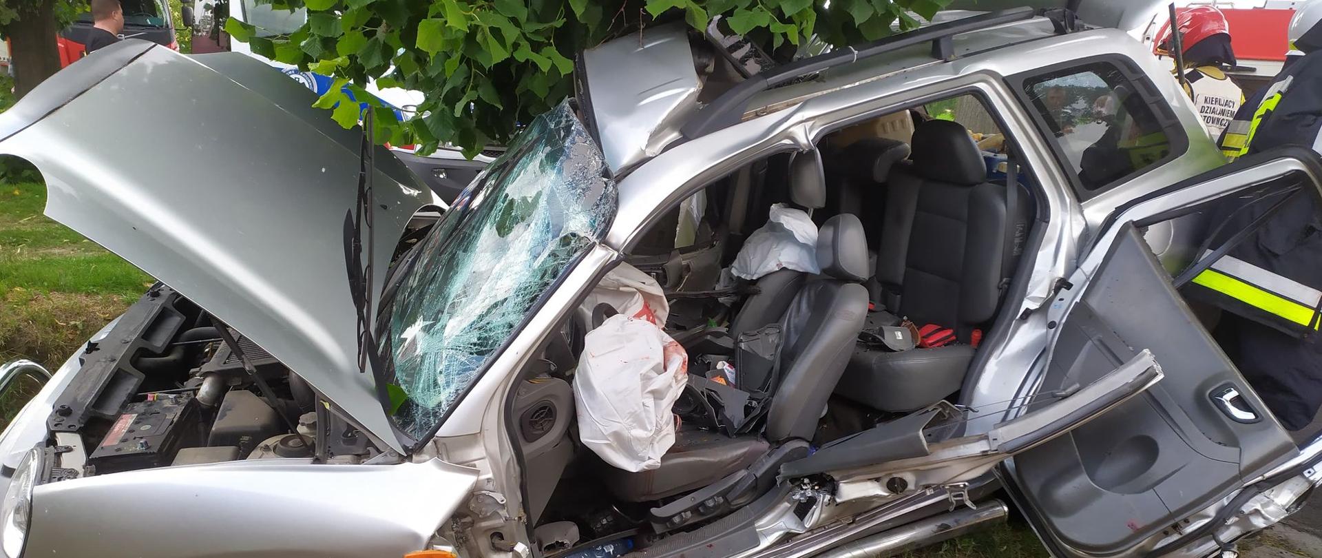 Zdjęcie przedstawia zdeformowana bryłę pojazdu po wcześniejszym wypadku. Pojazd koloru srebrnego typu SUV, ma wycięty środkowy słupek typu C oraz usunięte drzwi przednie lewe i tylne lewe.