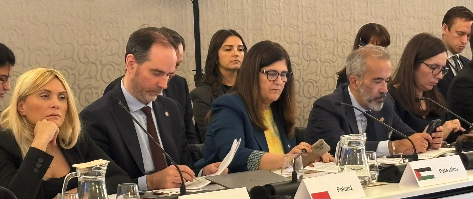 People during a meeting, a man in a suit drafting something in his notes.