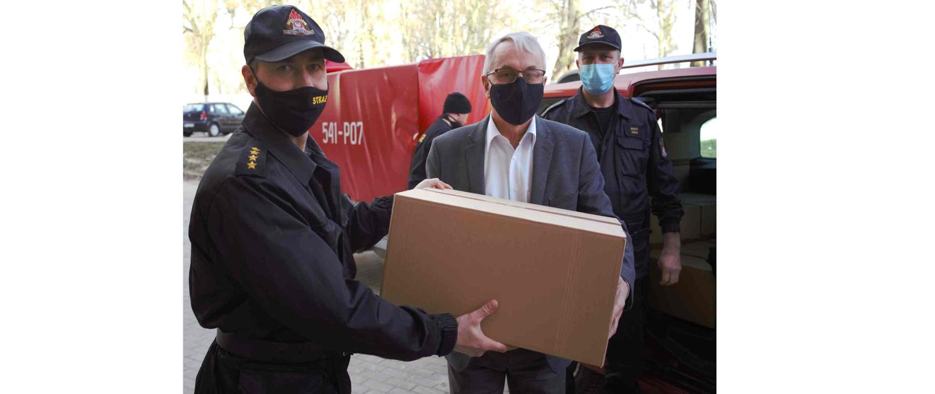 Strażak przekazujący karton z maseczkami urzędnikowi.