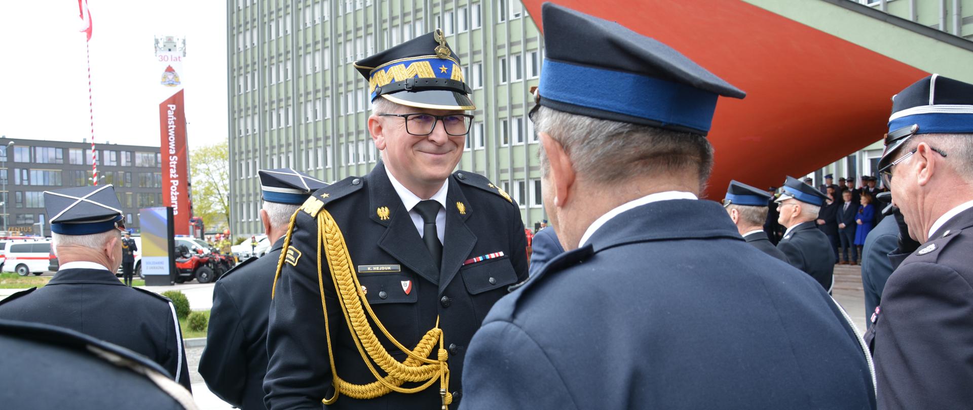 Na zdjęciu widzimy mężczyznę w mundurze generalskim PSP uśmiechającego się do stojącego tyłem strażaka OSP.