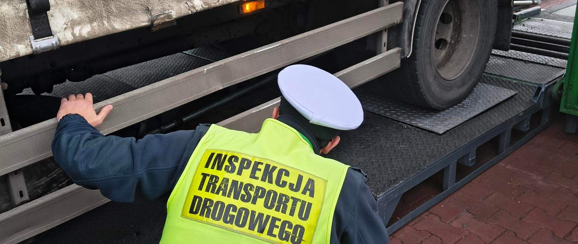 Inspektor w kamizelce odblaskowej zagląda pod przyczepę