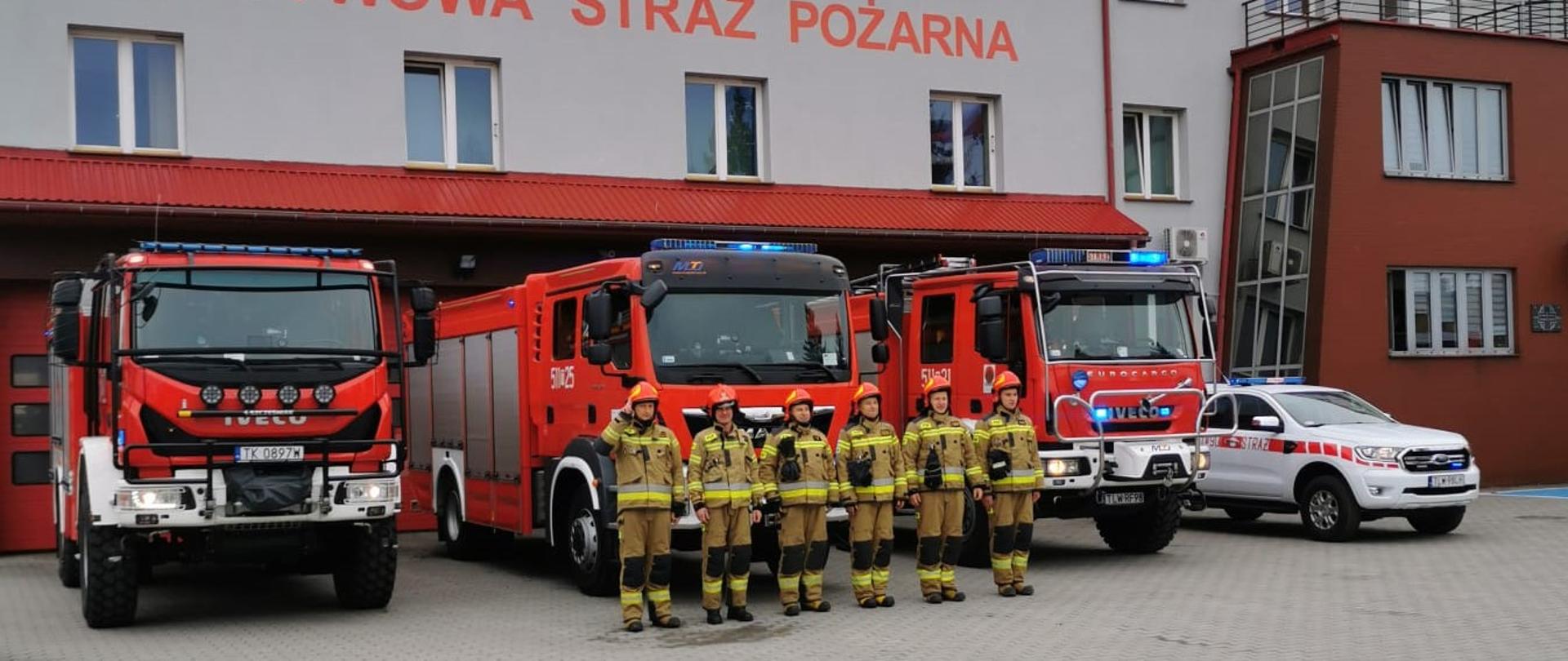 Zmiana służby w JRG Włoszczowa, zmiana służbowa ustawiona w szeregu przed pojazdami pożarniczymi przed budynkiem Komendy Powiatowej Państwowej Straży Pożarnej we Włoszczowie
