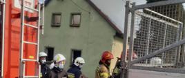 Na zdjęciu widać strażaków oraz wóz gaśniczy na tle palącego się budynku
