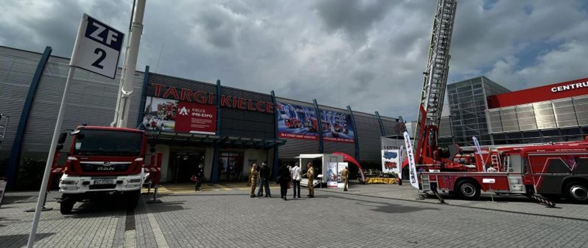 Widok na wejście na targi. Duża brama. Po bokach wozy strażackie.