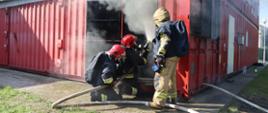 Zdjęcie przedstawia strażaków PSP z terenu województwa pomorskiego, operujących prądem gaśniczym w modułowym wielokontenerowym symulatorze do nauki i doskonalenia gaszenia pożarów wewnętrznych.