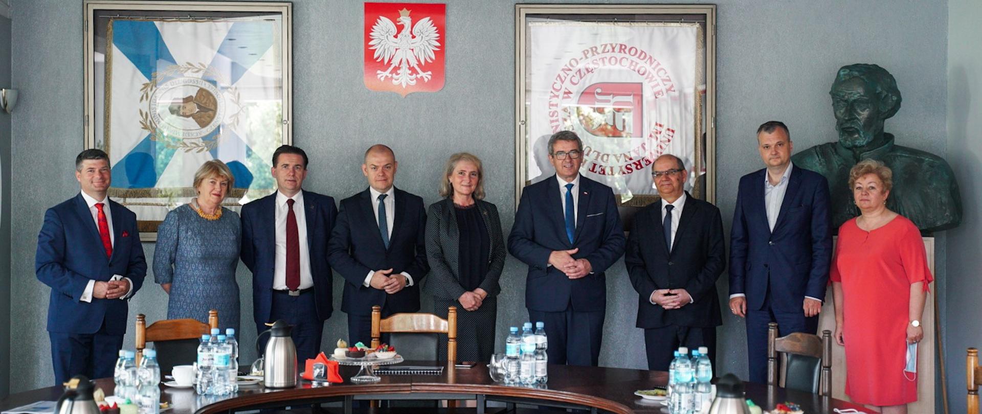 Minister i przedstawiciele UHP stoją za stołem, za nimi ściana z godłem Polski i sztandar uniwersytetu.