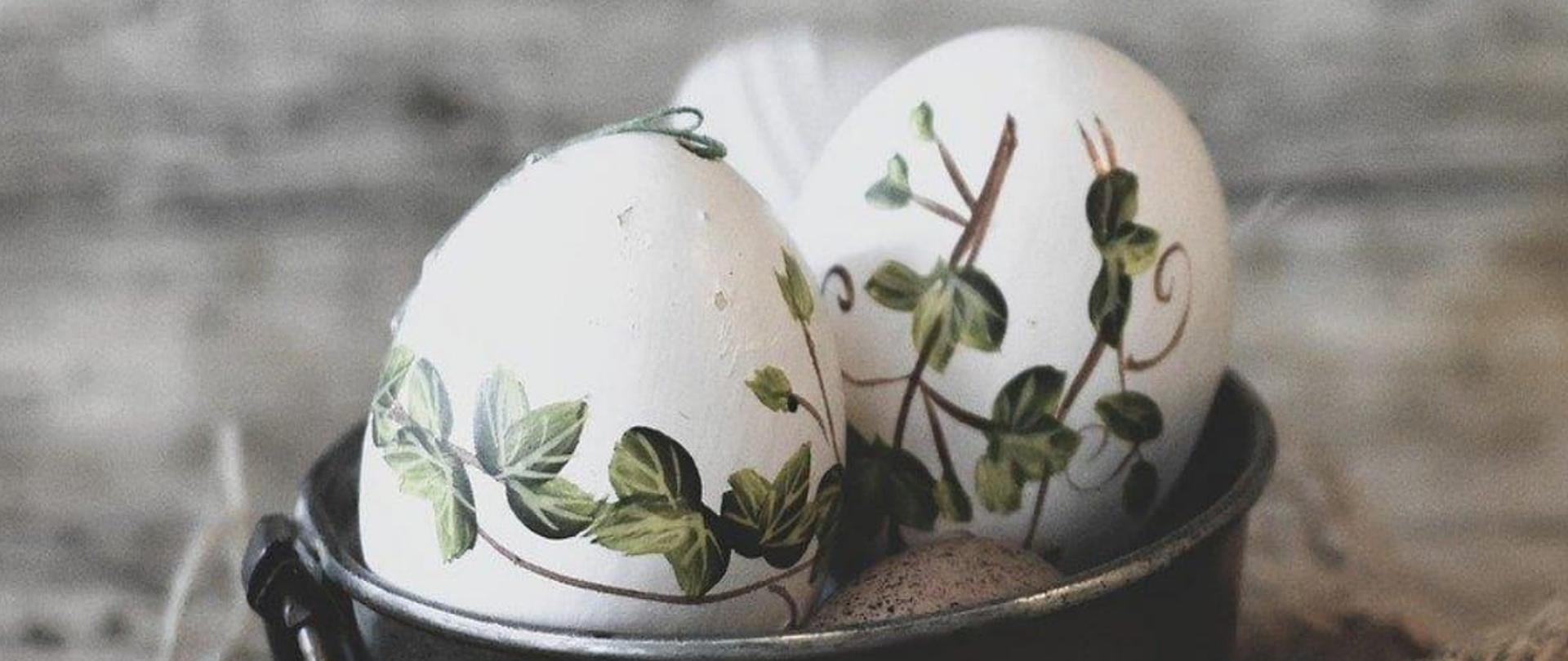 Na grafice na szarym tle znajduje się napis Radosnych świąt wielkiej nocy, pełnych miłości i nadziei, a także wielu okazji do miłych spotkań w gronie najbliższych, spokoju i wytchnienia od codzienności, życzą pracownicy i uczniowie państwowej szkoły muzycznej I stopnia im. Witolda Lutosławskiego w Jaśle, w dolnym lewym rogu białe pisanki z motywem roślinnym w koszyczku, pleciona tkanina, w prawym dolnym rogu logo szkoły