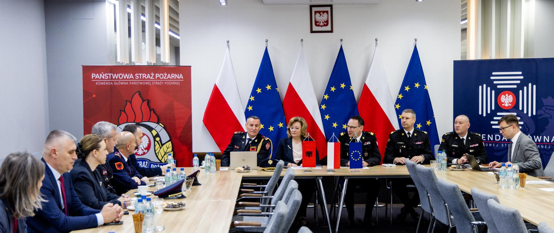 Delegacje siedzą przy długich stołach podczas spotkania w Komendzie Głównej Państwowej Straży Pożarnej; w tle widoczne flagi Polski i Unii Europejskiej oraz banery PSP.