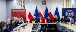 Delegacje siedzą przy długich stołach podczas spotkania w Komendzie Głównej Państwowej Straży Pożarnej; w tle widoczne flagi Polski i Unii Europejskiej oraz banery PSP.