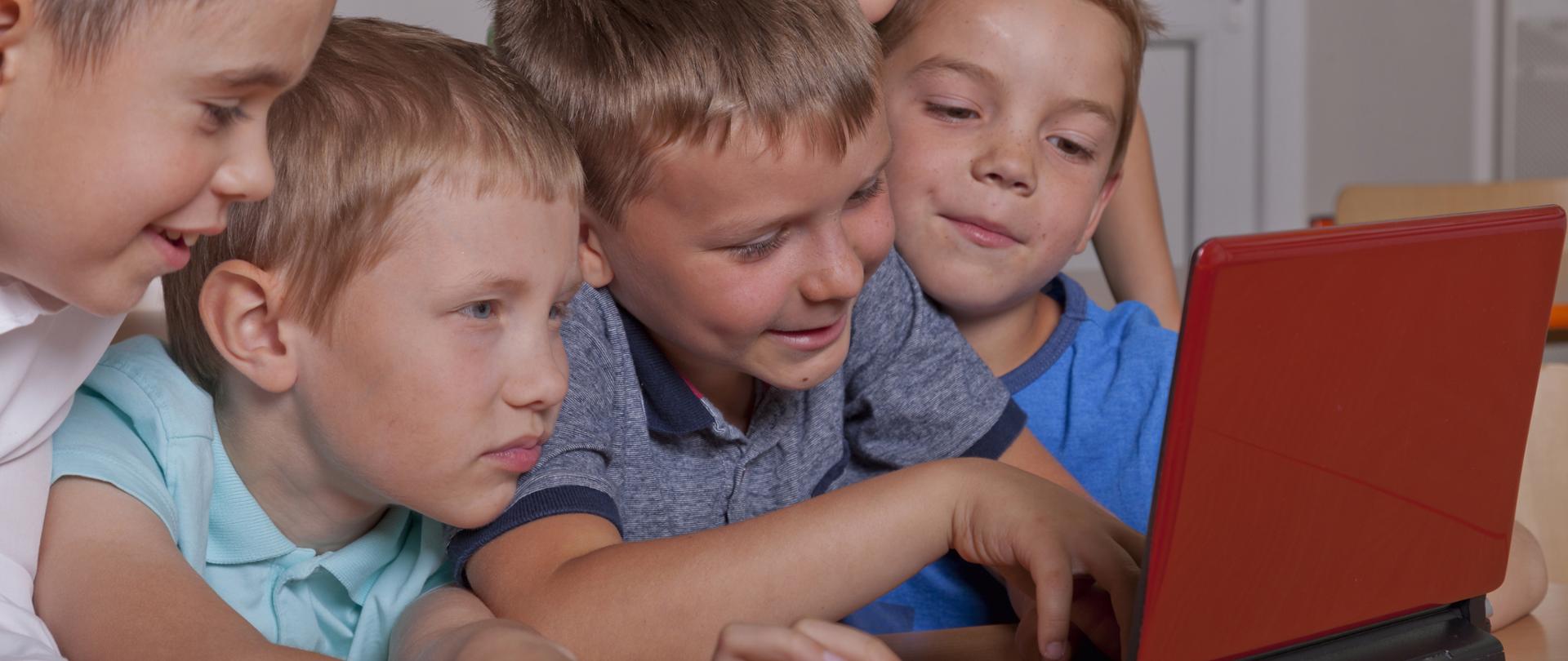 Uśmiechnięte dzieci siedzą przy komputerze 