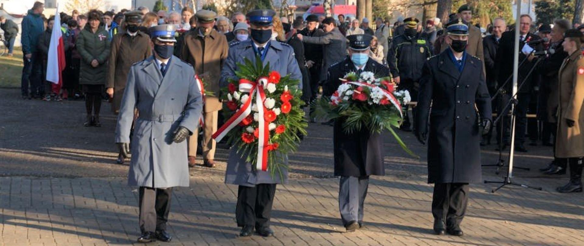 Na tle zgromadzonych ludzi delegacja czterech funkcjonariuszy w zimowym umundurowaniu galowym, dwóch z nich trzyma wieńce.