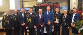 komendanci oraz politycy i przedstawiciele samorządu pozują do zdjęcia w tle stoi lekki samochód strażacki iveco ozdobiony biało-czerwonymi wstęgami