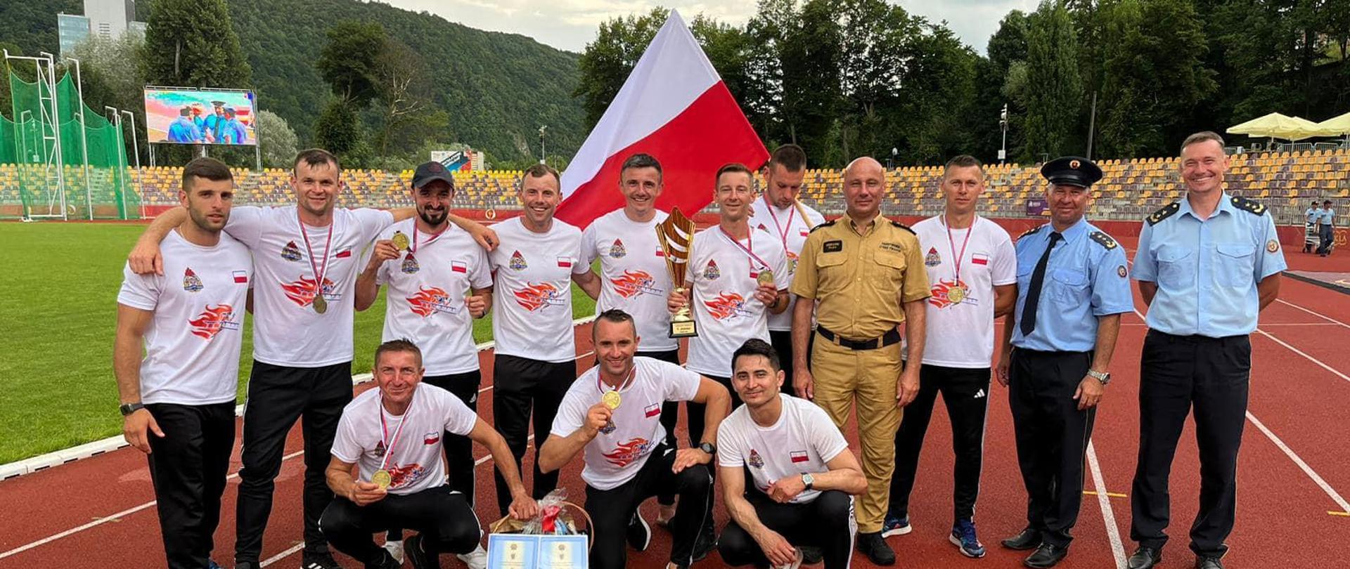 Na zdjęciu strażacy pozują z nagrodami i medalami na arenie sportowej po ceremonii wręczenia nagród.