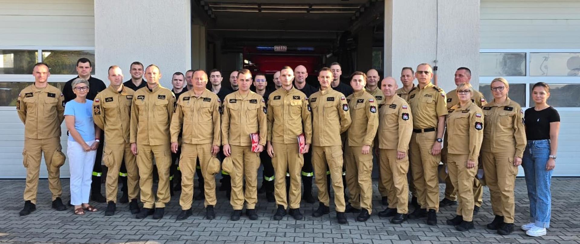 grupa strażaków w ubraniach służbowych stojący przed komendą 