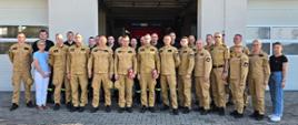 grupa strażaków w ubraniach służbowych stojący przed komendą 