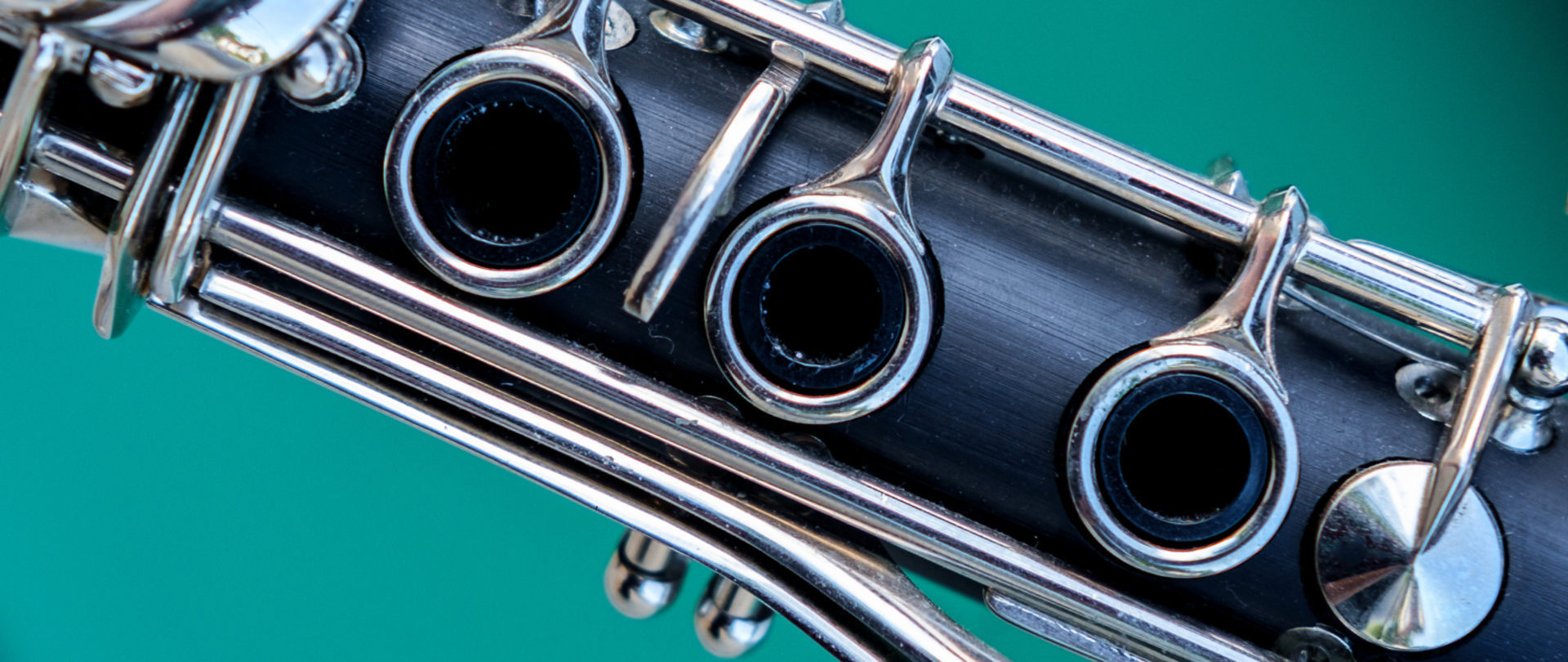 Kolorowe zdjęcie środkowej części klarnetu z klapkami, znajdującego się na turkusowym tle.