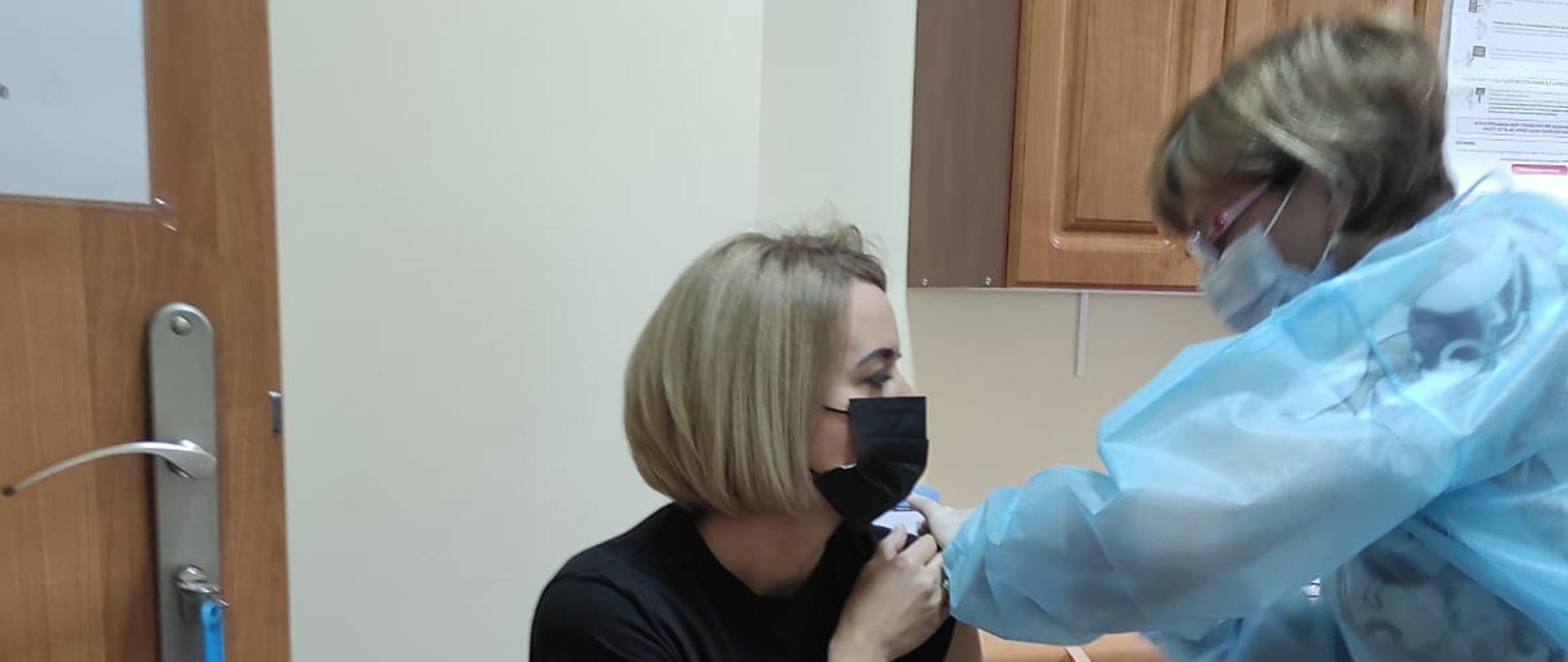 Funkcjonariuszka PSP na krześle podczas przyjmowania szczepienia.