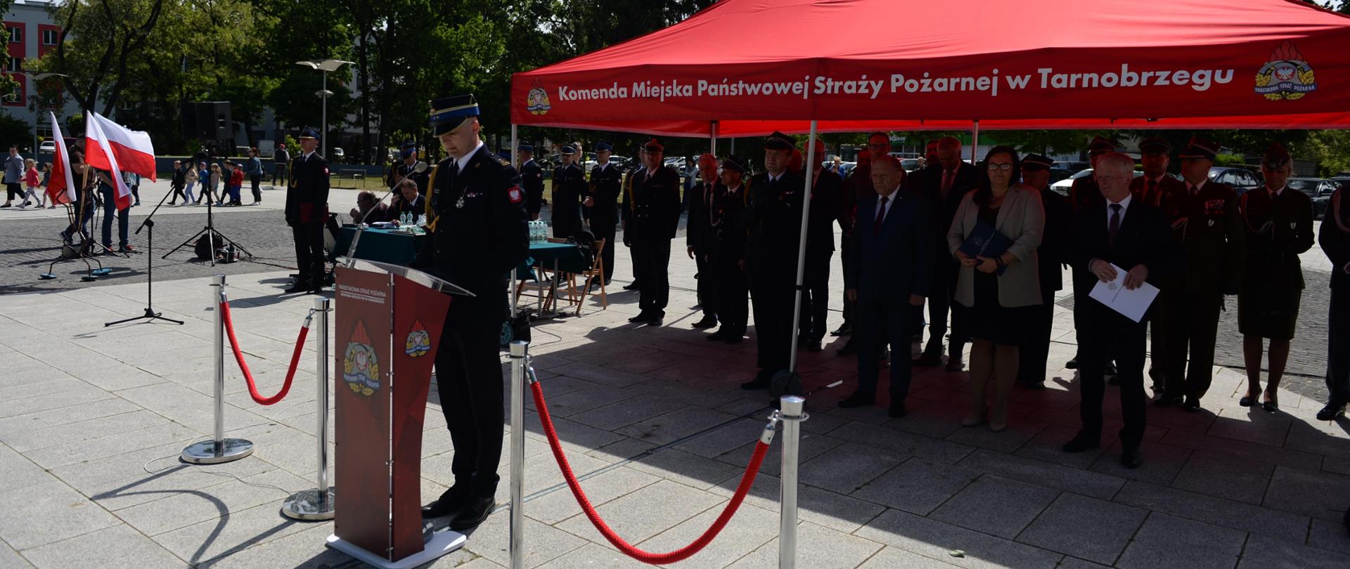 Strażak przemawia, za nim goście honorowi 