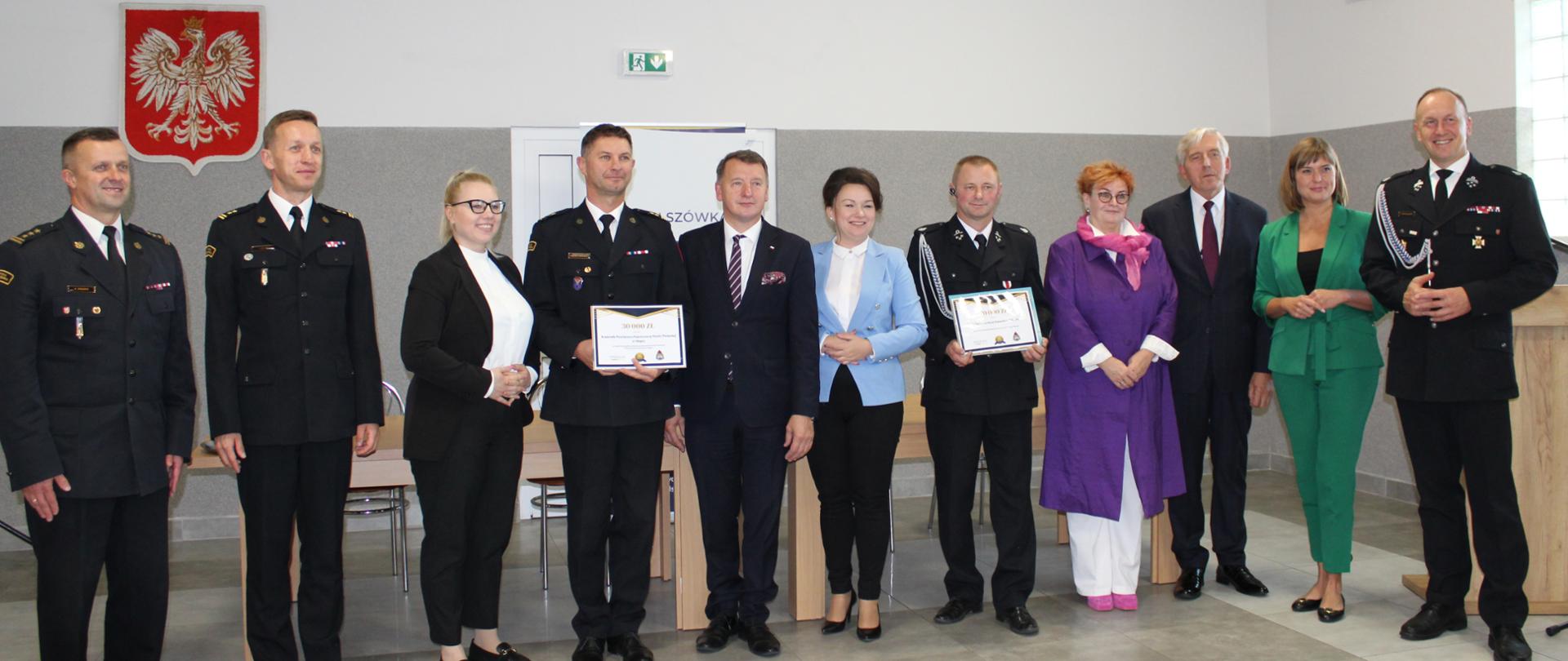 zdjecie grupowe kobiet, i mężczyzn, wśród nich strażacy, w tle godło polski