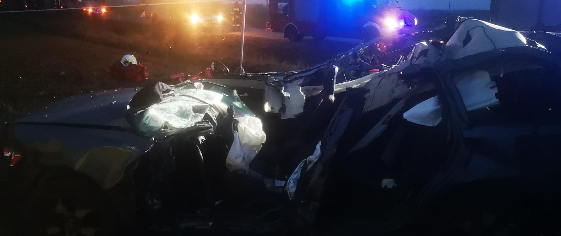 Uszkodzony samochód po wypadku, w tle straż pożarna