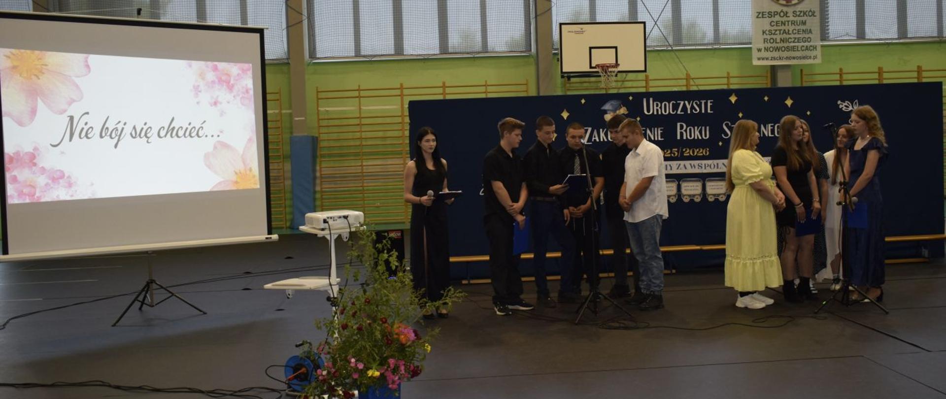 Uczniowie ZSCKR Nowosielce w trakcji programu artystycznego zakończenia Roku szkolnego 2025/2026. W tle widać ściankę promującą wydarzenie . Projektor wyświetla napis: "Nie bój się chcieć..."