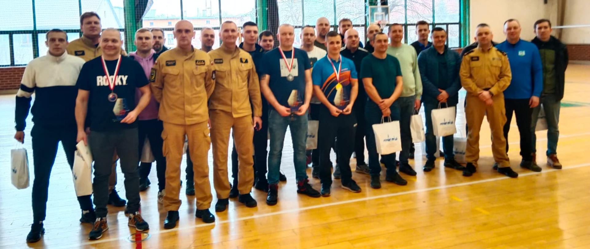 Zdjęcie grupowe strażaków biorących udział w mistrzostwach w tenisie stołowym wraz z Zastępcą Komendanta Powiatowego PSP w Kłodzku oraz Naczelnikiem Ośrodka Szkolenia Komendy Wojewódzkiej PSP we Wrocławiu. 