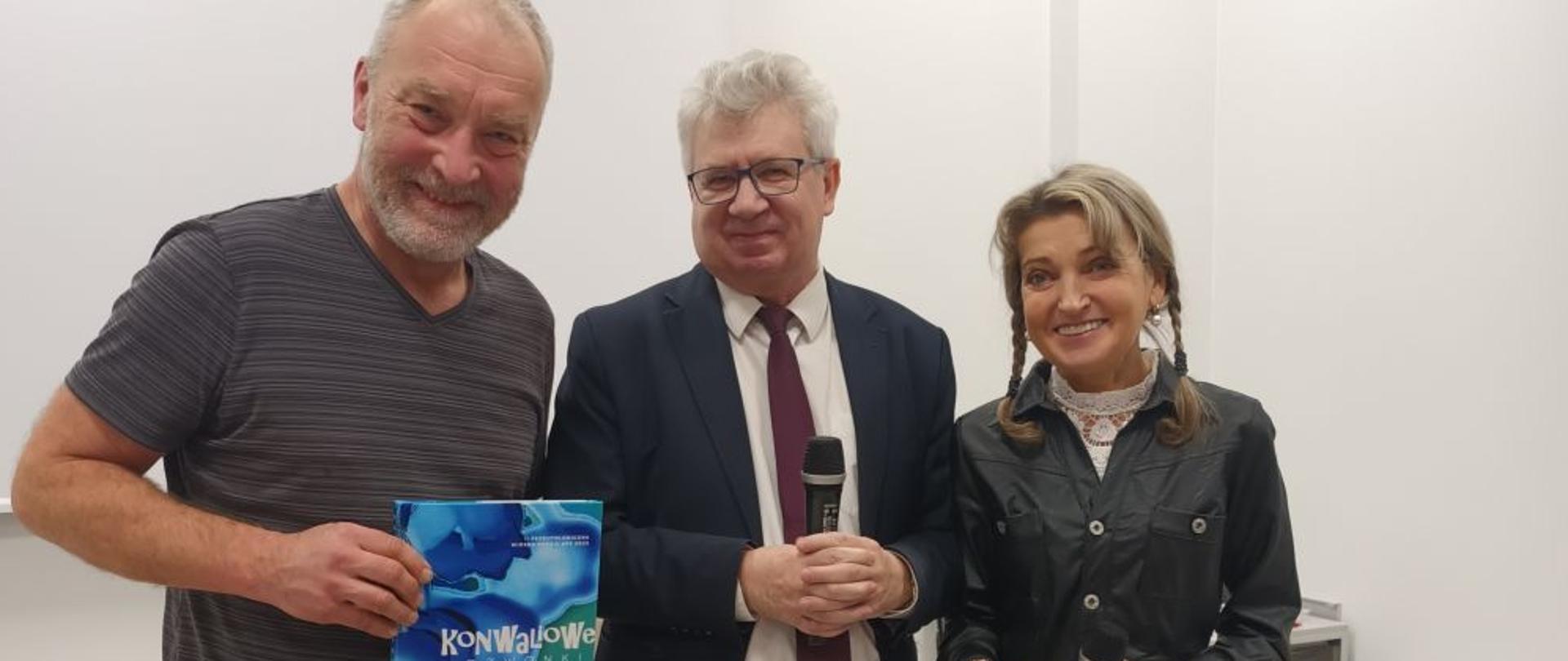 Na zdjęciu znajdują się trzy postacie. Pierwsza od lewej: dr Piotr Bies laureat konkursu. Piotr Bies trzyma w rękach tomik poezji. W środku stoi dr hab. Jarosław Michalski prof. Akademii Pedagogiki Specjalnej w Warszawie, a po prawej stronie stoi dr Beata Szurowska.