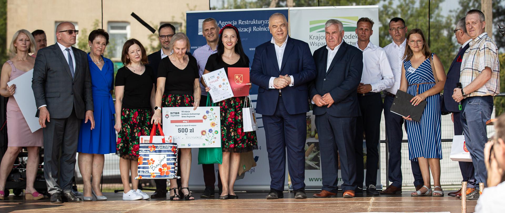Na zdjęciu wicepremier Jacek Sasin wśród grupy ludzi. Poniżej napis Bitwa, VII edycja konkursu kulinarnego dla kół.