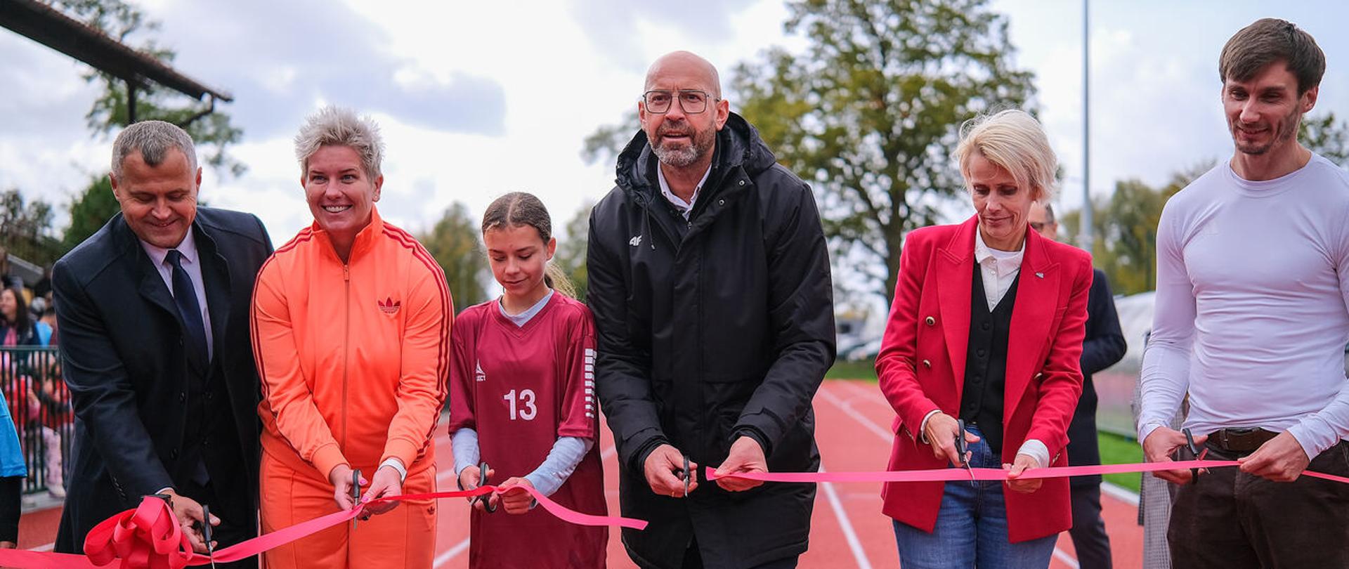Minister sportu i Turystyki w Gostyninie. Przecina różową wstęgę stojąc w czarnej kurtce na tle stadionu