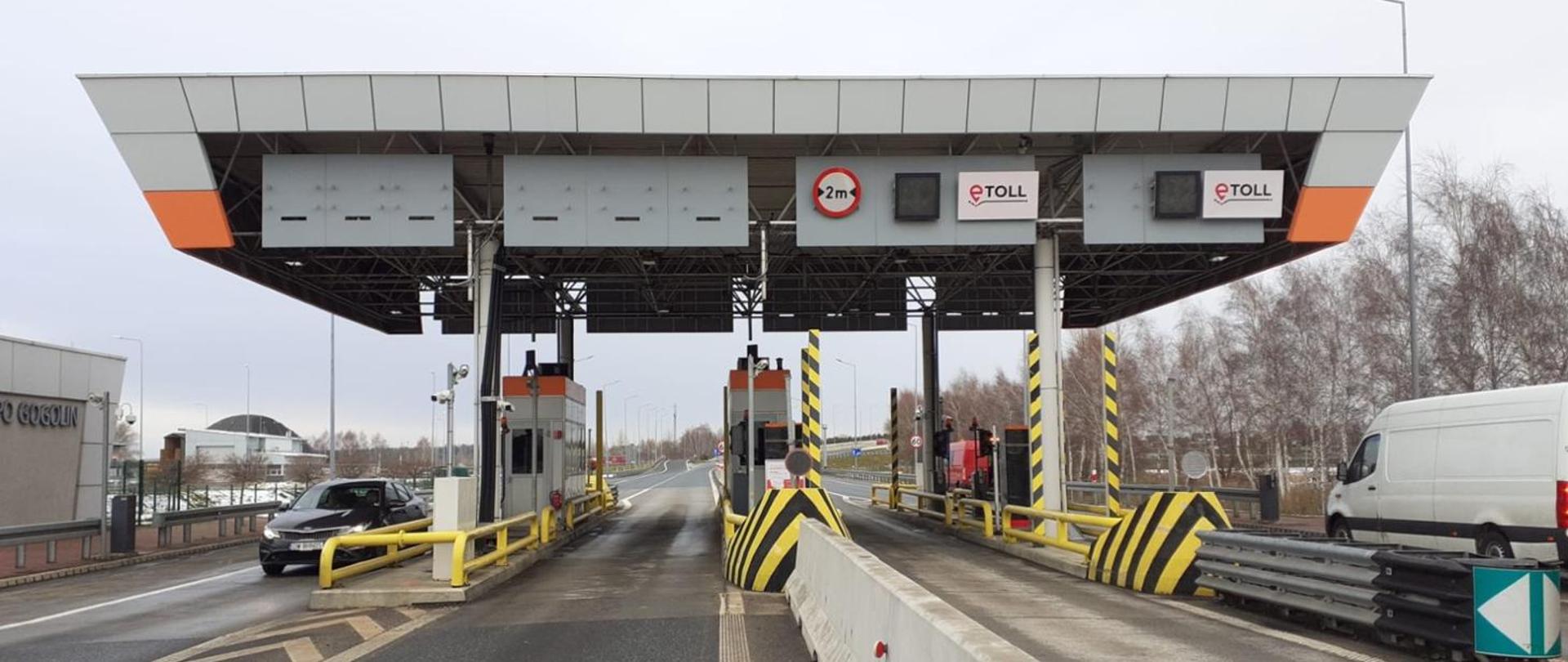 Stacja poboru opłat na autostradzie A4 – widok na kilka pasów zadaszonych bramek z oznaczeniami e‑TOLL, zapory drogowe i znaki ograniczenia wysokości; brak obsługi i otwarte przejazdy.