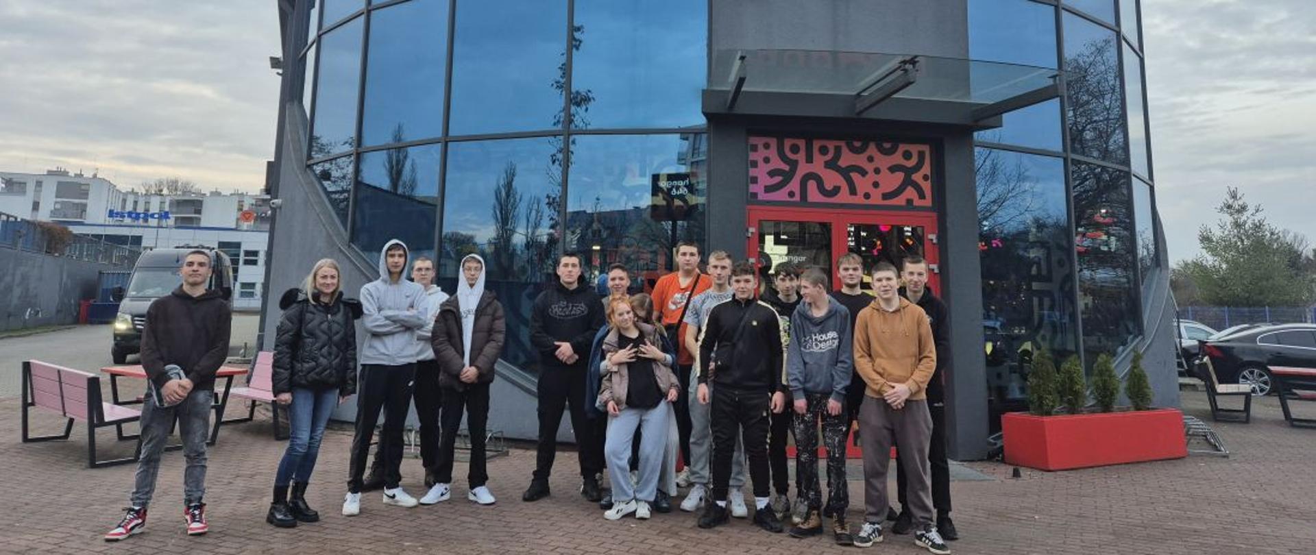 Grupa uczniów z opiekunką stoi pod budynkiem oznaczonym Hangar 646