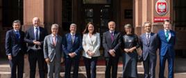 Na zdjęciu podsekretarz stanu Anny Radwan-Röhrenschef z grupą ośmiu osób. Stoją przed budynkiem MSZ.