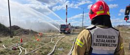 Działania gaśnicze, woda leje się z dział. Na pierwszym planie widać strażaka, na kamizelce ma napis Kierujący Działaniem Gaśniczym.