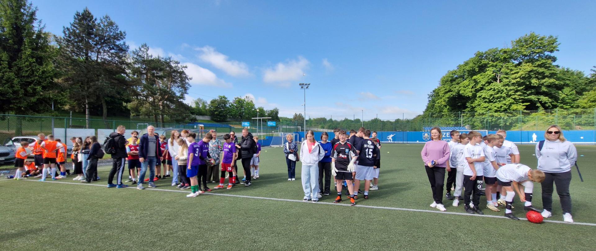 Młodzieżowe drużyny piłkarskie stojące na boisku wzdłuż linii bocznej