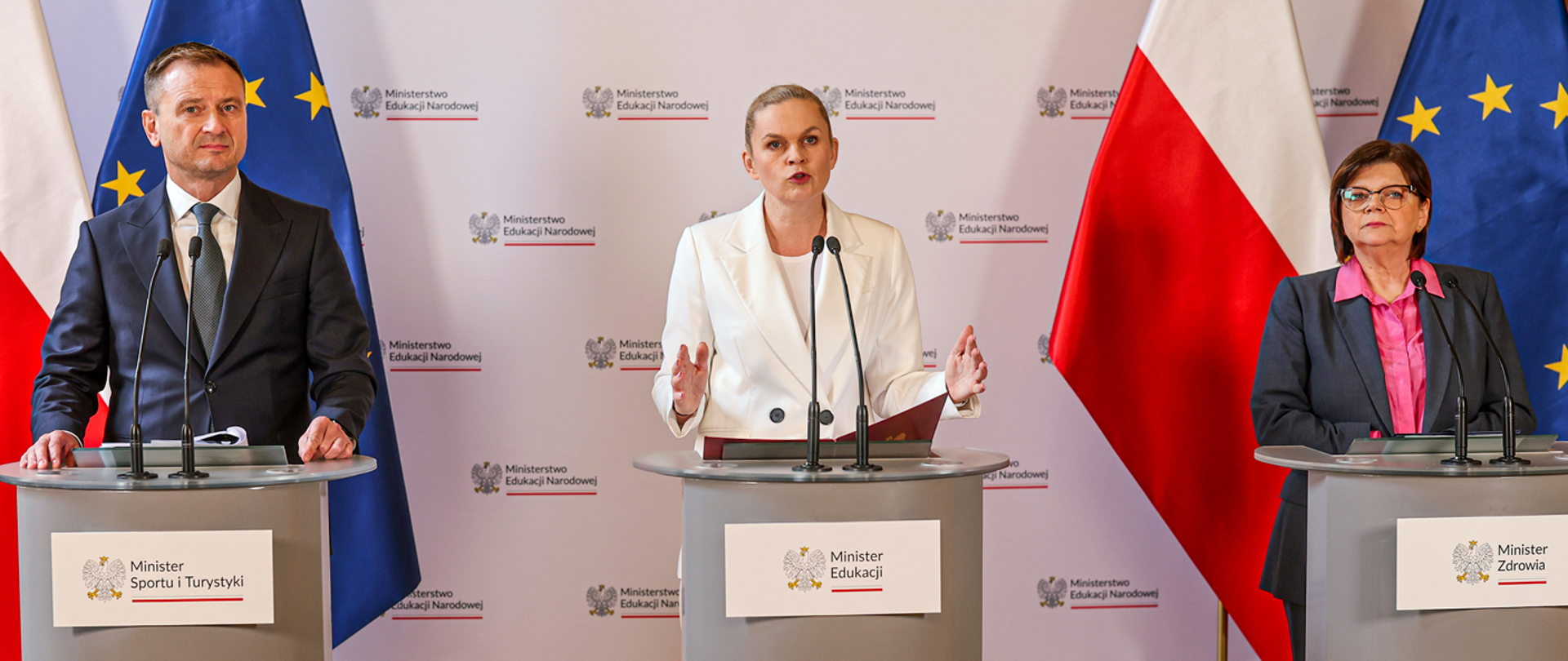 Konferencja prasowa. Od lewej: Minister Sportu i Turystyki Sławomir Nitras, Minister Edukacji Barbara Nowacka, Minister Zdrowia Izabela Leszczyna. W tle ścianka z logotypem MEN. Z tyłu z obu stron flagi Polski i UE.
