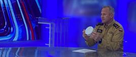 Za stołem w studio telewizyjnym komendant wojewódzki w mundurze służbowym. W ręku trzyma czujnik czadu - trwa prezentacja.